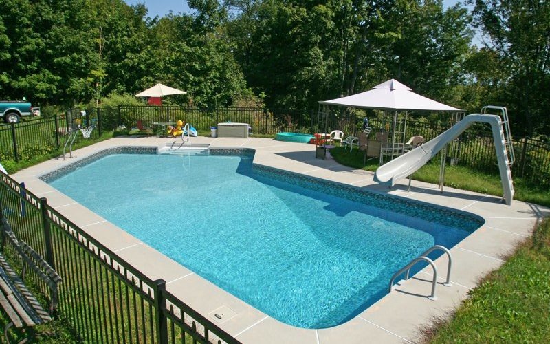 This is a photo of a Lazy L style custom inground swimming pool with a black fence, steps and water slide.